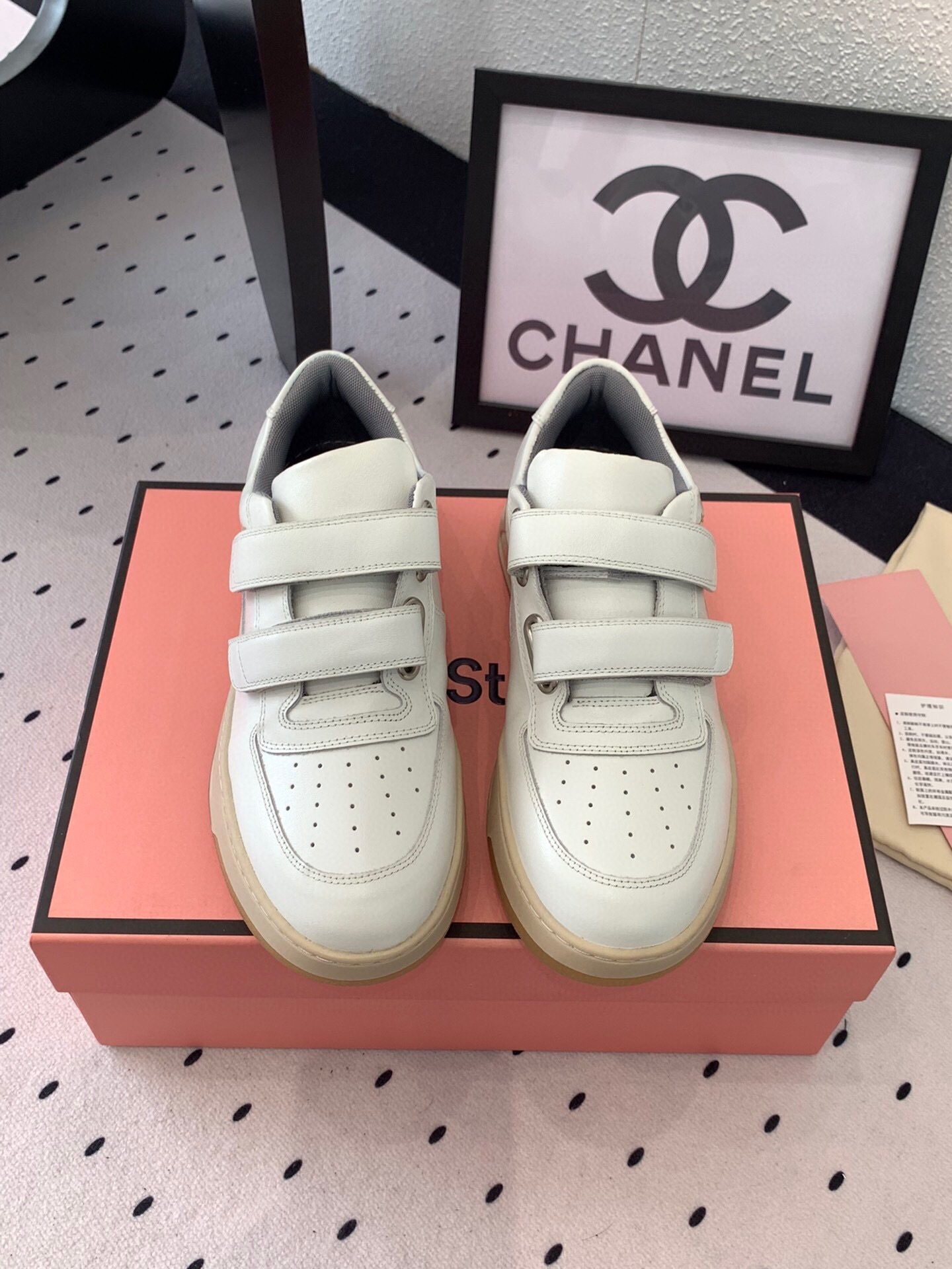 White Acne Studios Perey leather sneakers with triple velcro straps and signature face motif on the heel, displayed on a pink box.
